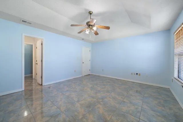 an empty room with chandelier fan and windows