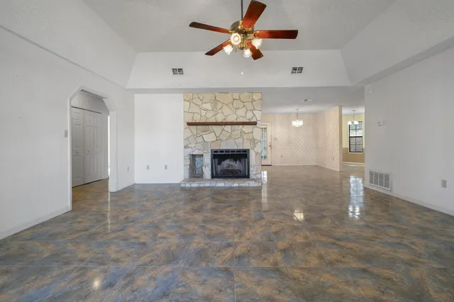 an empty room with chandelier fan and fireplace