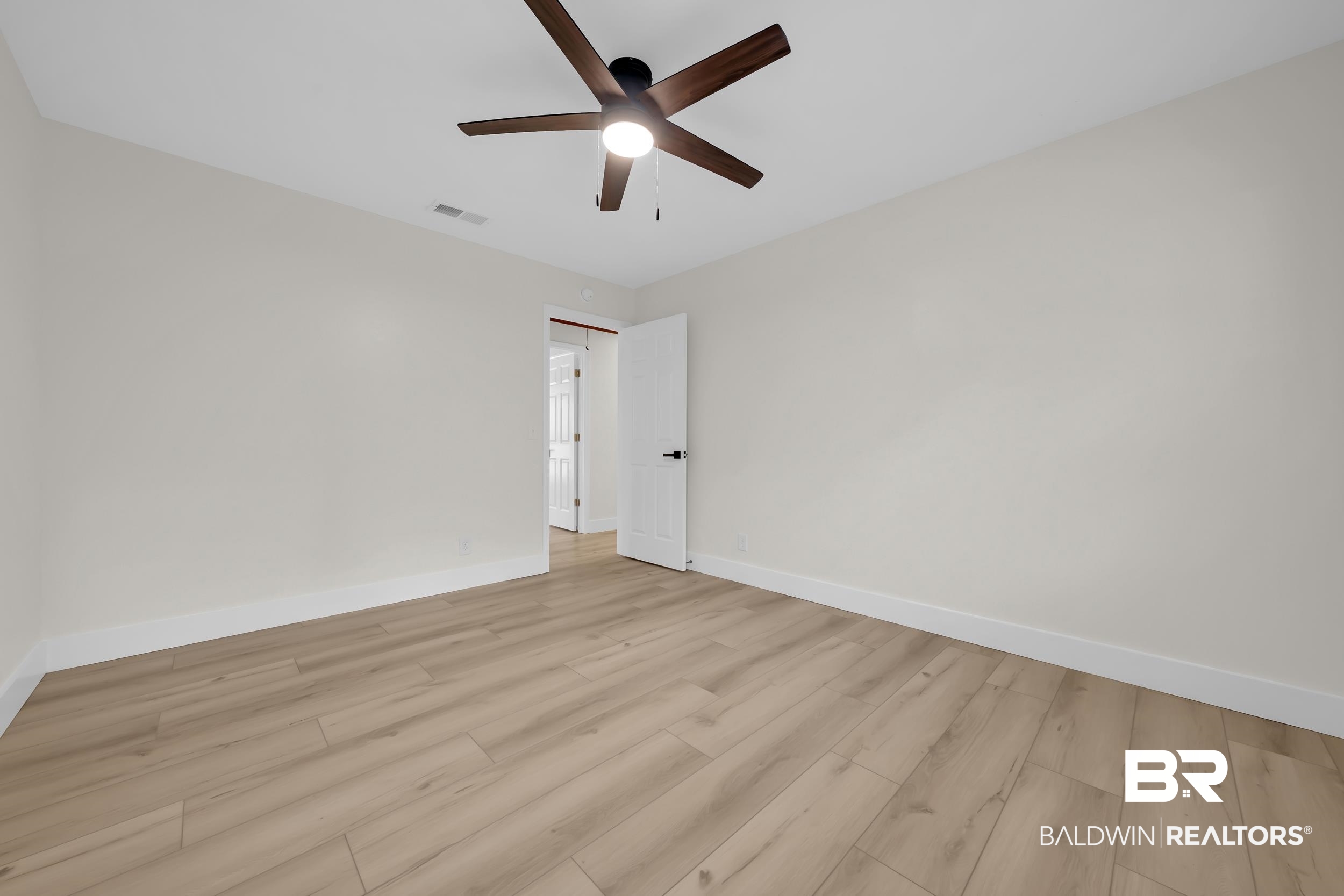 8170 Wilmer Georgetown Road Wilmer, AL 36587 - Photo 17 of 31 Spacious room featuring light wood-finish flooring, a modern ceiling fan with wood-look blades, white baseboards, and a white interior door with black hardware