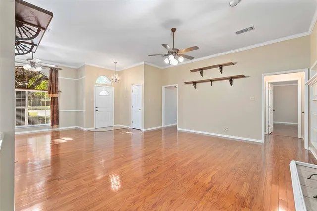 a view of an empty room with wooden floor ceiling fan