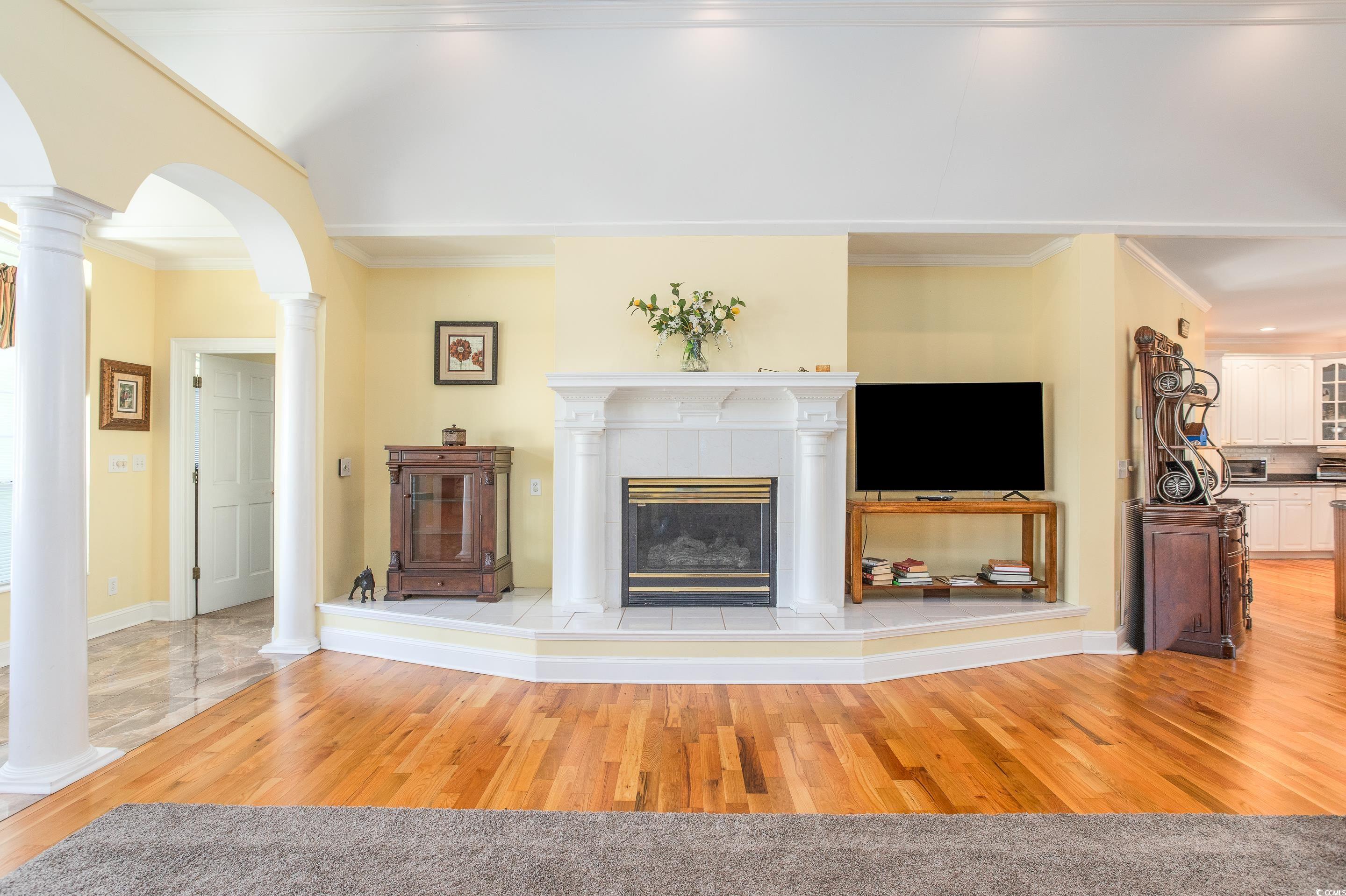 4907 Woodview Lane Myrtle Beach, SC 29575 - Photo 10 of 30 Living area with wood finished floors, arched walkways, ornamental molding, ornate columns, and a tiled fireplace