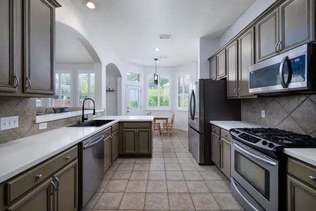 a kitchen with stainless steel appliances granite countertop a sink a stove a refrigerator cabinets and a microwave