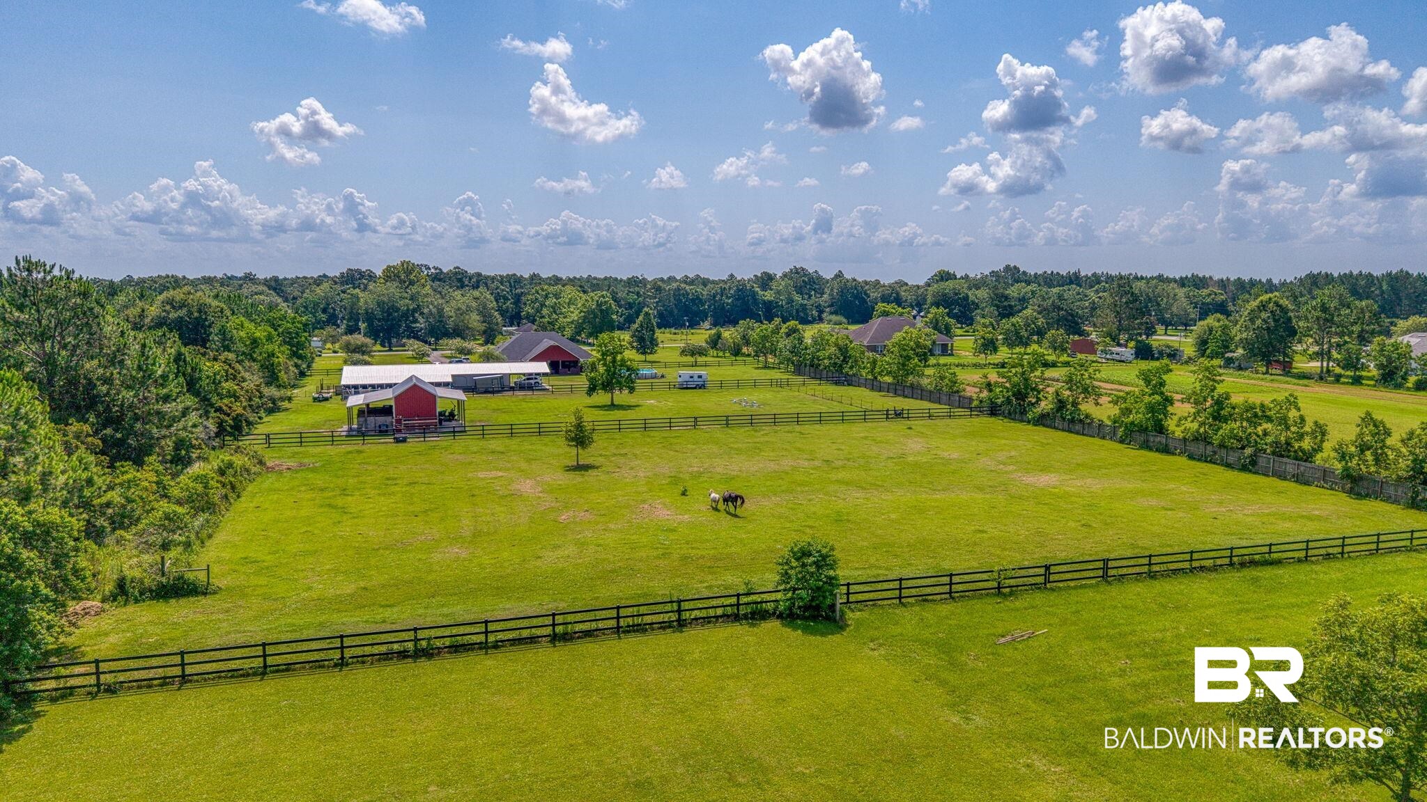 26895 C R Watson Road Robertsdale, AL 36567 - Photo 6 of 89 Expansive green pastureland with perimeter fencing, featuring multiple outbuildings including a red barn with an attached covered structure, and a secondary residential structure