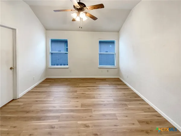 an empty room with wooden floor fan and windows