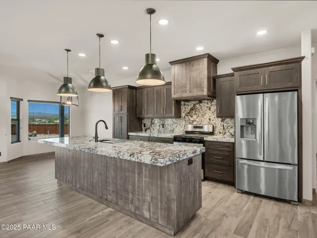 a large kitchen with stainless steel appliances granite countertop a stove a refrigerator and a sink with wooden floor