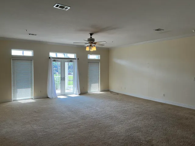 an empty room with chandelier fan and windows