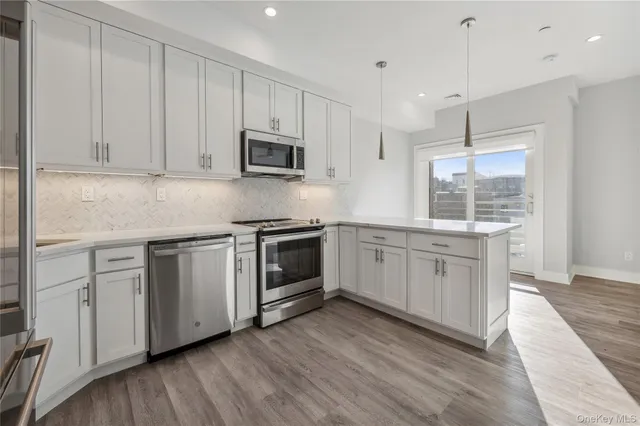 a kitchen with stainless steel appliances granite countertop white cabinets a sink a stove a refrigerator and microwave with wooden floor