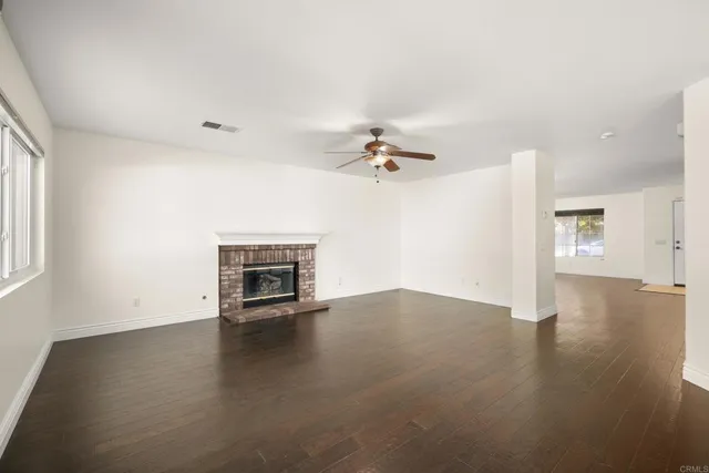 an empty room with wooden floor fireplace and windows