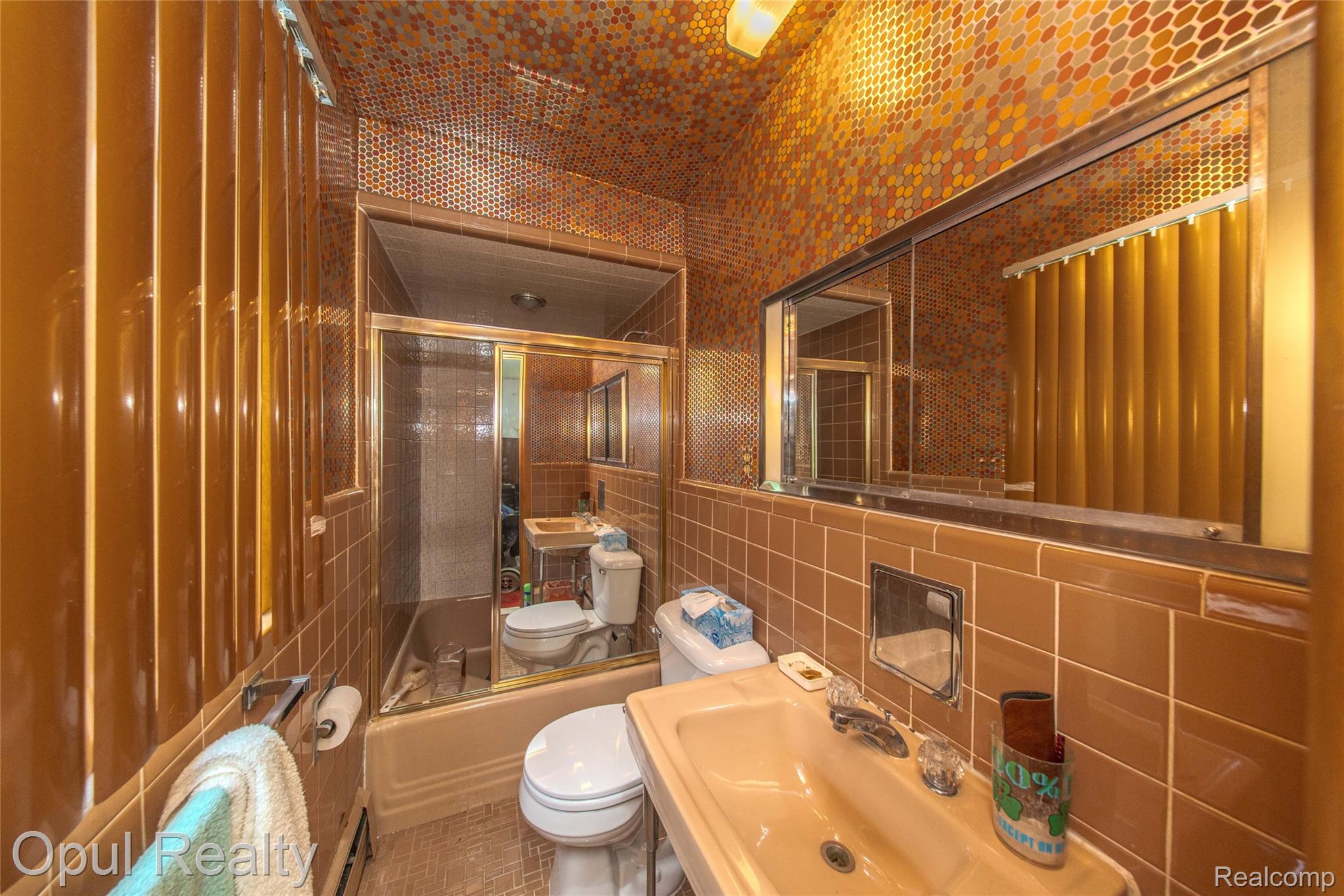 6455 Norham Road Bloomfield Hills, MI 48301 - Photo 57 of 93 Bathroom featuring extensive brown tilework, a built-in bathtub with a sliding glass enclosure, and a wall-mounted vanity mirror