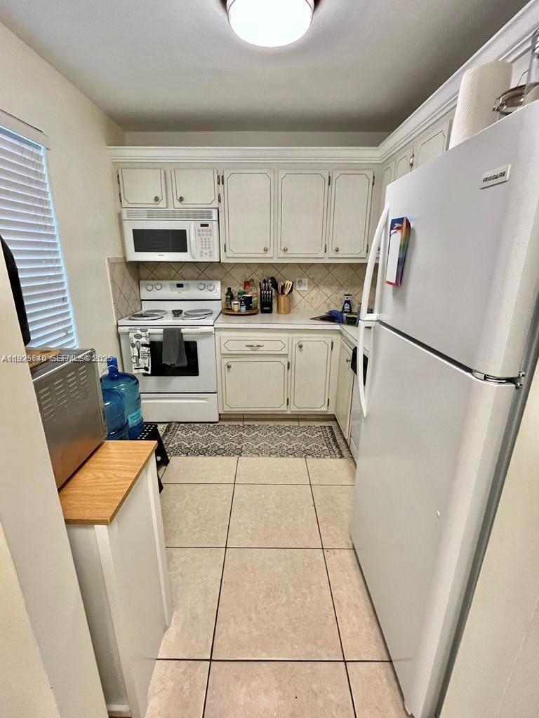 5961 Northwest 61st Avenue, Unit 208 Tamarac, FL 33319 - Photo 6 of 11 a kitchen with a refrigerator a stove top oven and white cabinets