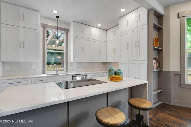 a kitchen with stainless steel appliances granite countertop a sink a window and white cabinets