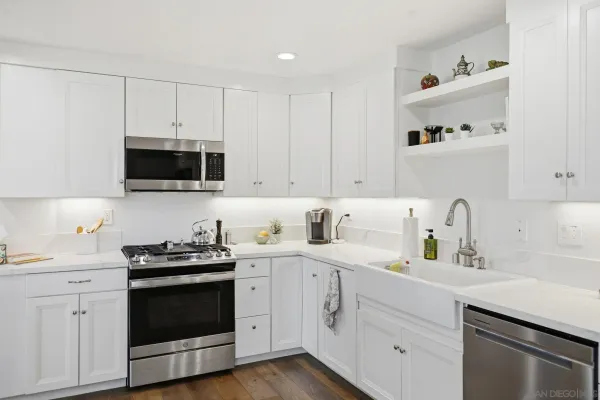 a kitchen with stainless steel appliances a sink a stove a refrigerator cabinets and a dining table with wooden floor