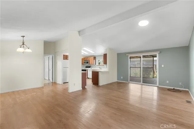 an empty room with wooden floor kitchen view and windows