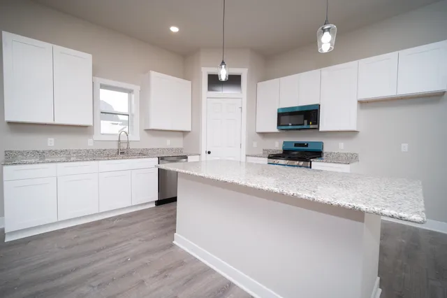 a kitchen with granite countertop a refrigerator a sink a stove a microwave and wooden floor