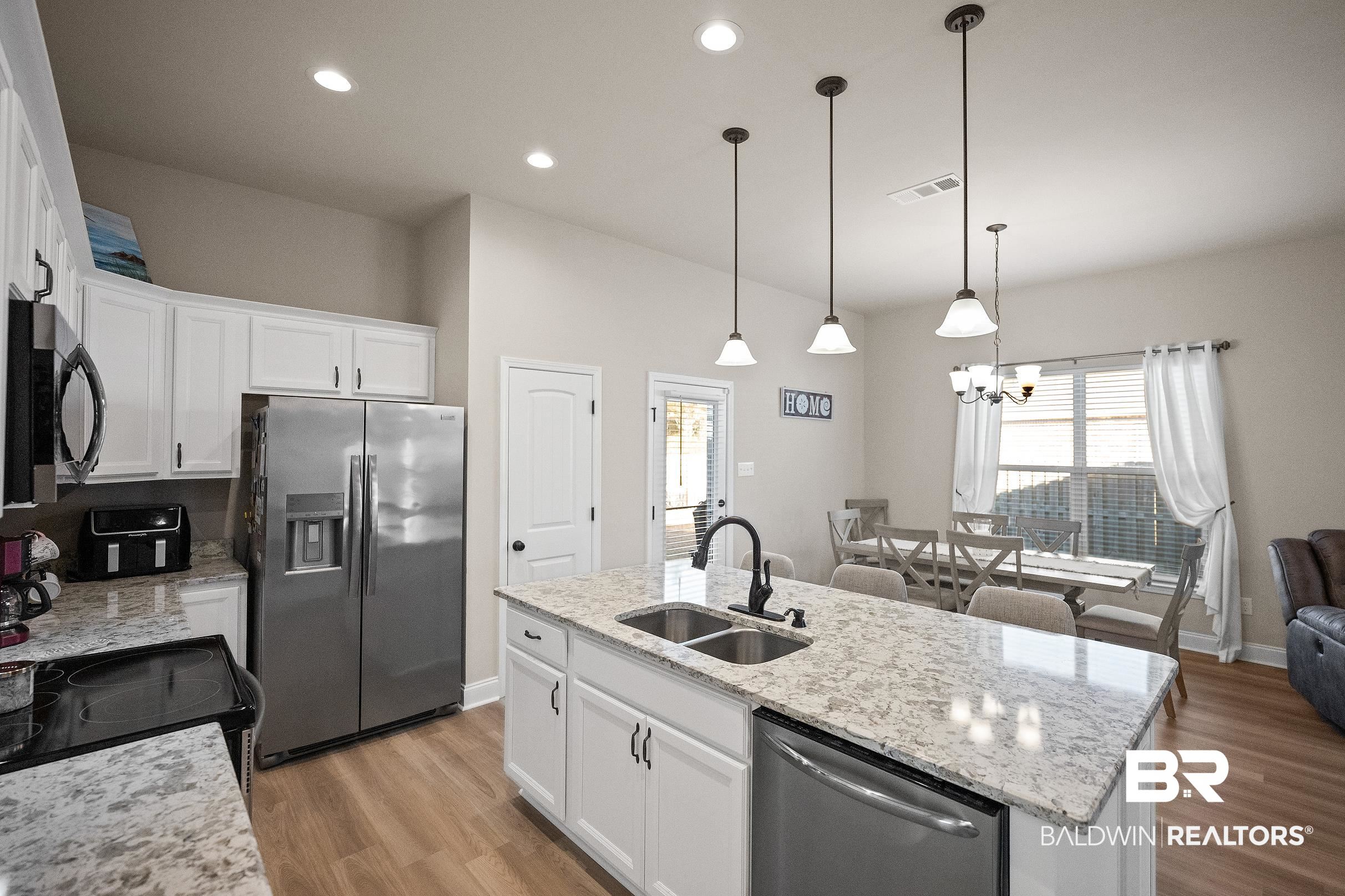 1077 Stella Road Foley, AL 36535 - Photo 12 of 27 Kitchen featuring white cabinets, black appliances, light wood-style flooring, light stone counters, and a kitchen island with sink