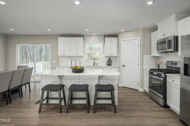 a kitchen with a dining table chairs appliances wooden floor and cabinets