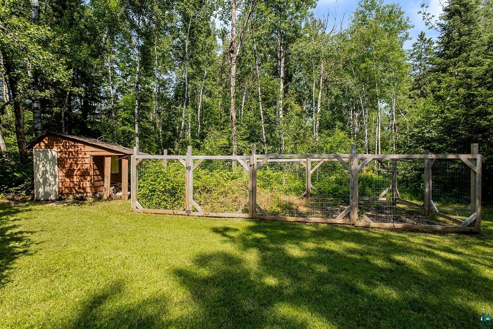 29 Ridge Road Esko, MN 55733 - Photo 5 of 41 Garden area featuring a wood-sided shed with a white door, a natural wood-framed fenced enclosure, and a dense tree line backdrop