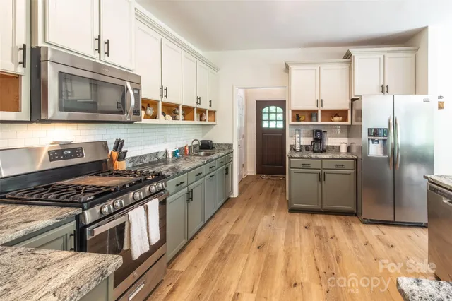 a kitchen with stainless steel appliances granite countertop a stove top oven a sink dishwasher a refrigerator and cabinets with wooden floor