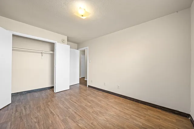 a view of an empty room with wooden floor and closet