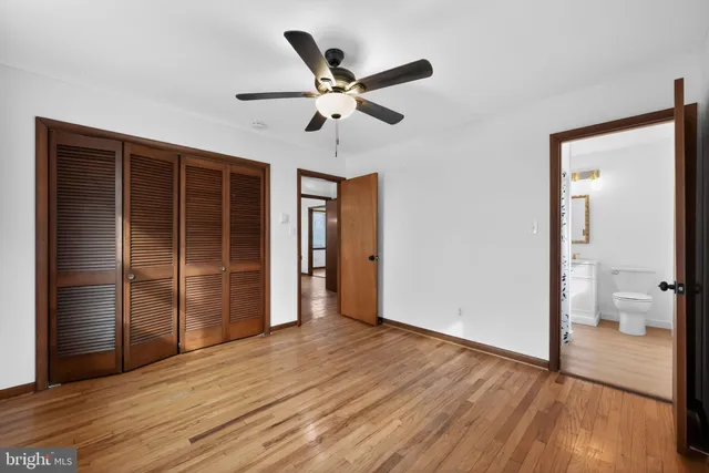 a view of an empty room with wooden floor and a ceiling fan