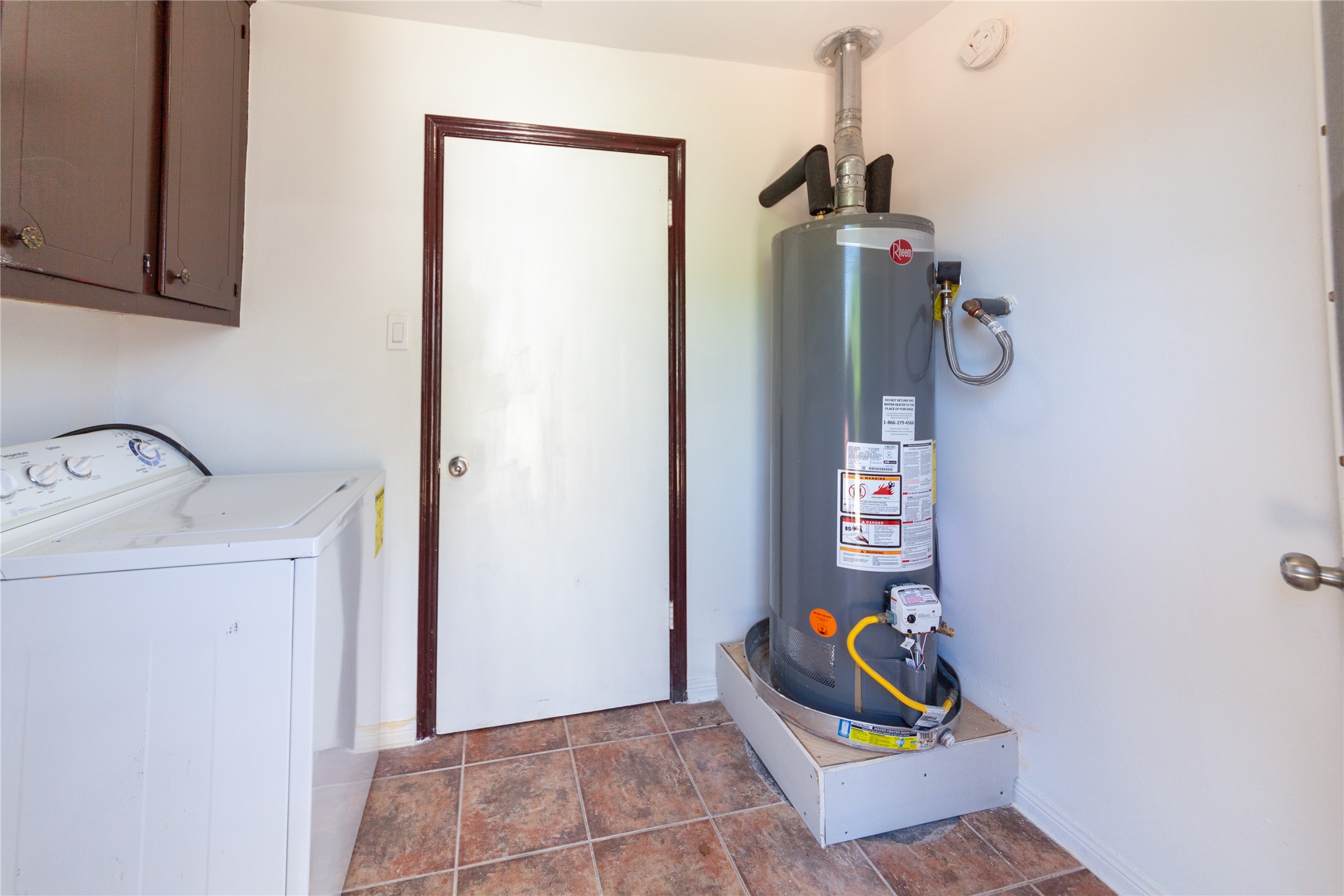 8826 Roos Road Houston, TX 77036 - Photo 34 of 42 A utility room with a water heater, washer, and cabinet space. The room features tiled flooring and a door leading to another area of the home.