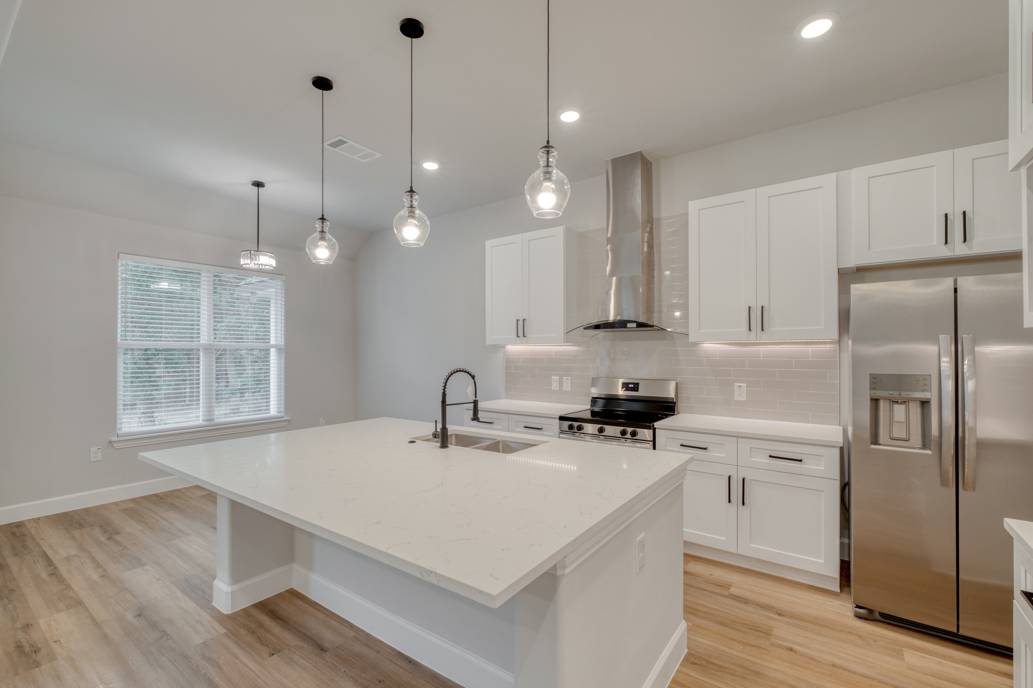 116 Pine Point Cove Elgin, TX 78621 - Photo 9 of 27 Modern kitchen featuring a large island with a double basin sink, stainless steel appliances, white shaker cabinetry, and wood-finish flooring