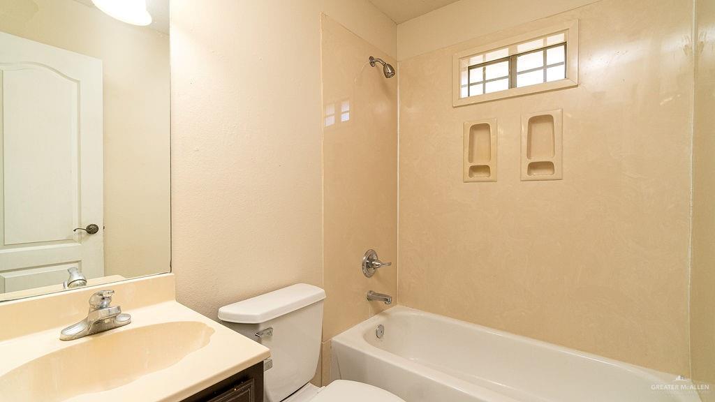 919 Hill Country Road Edinburg, TX 78539 - Photo 9 of 22 Bathroom featuring a vanity with an integrated sink and chrome faucet, a white toilet, and a bathtub with a shower head and built-in shelving