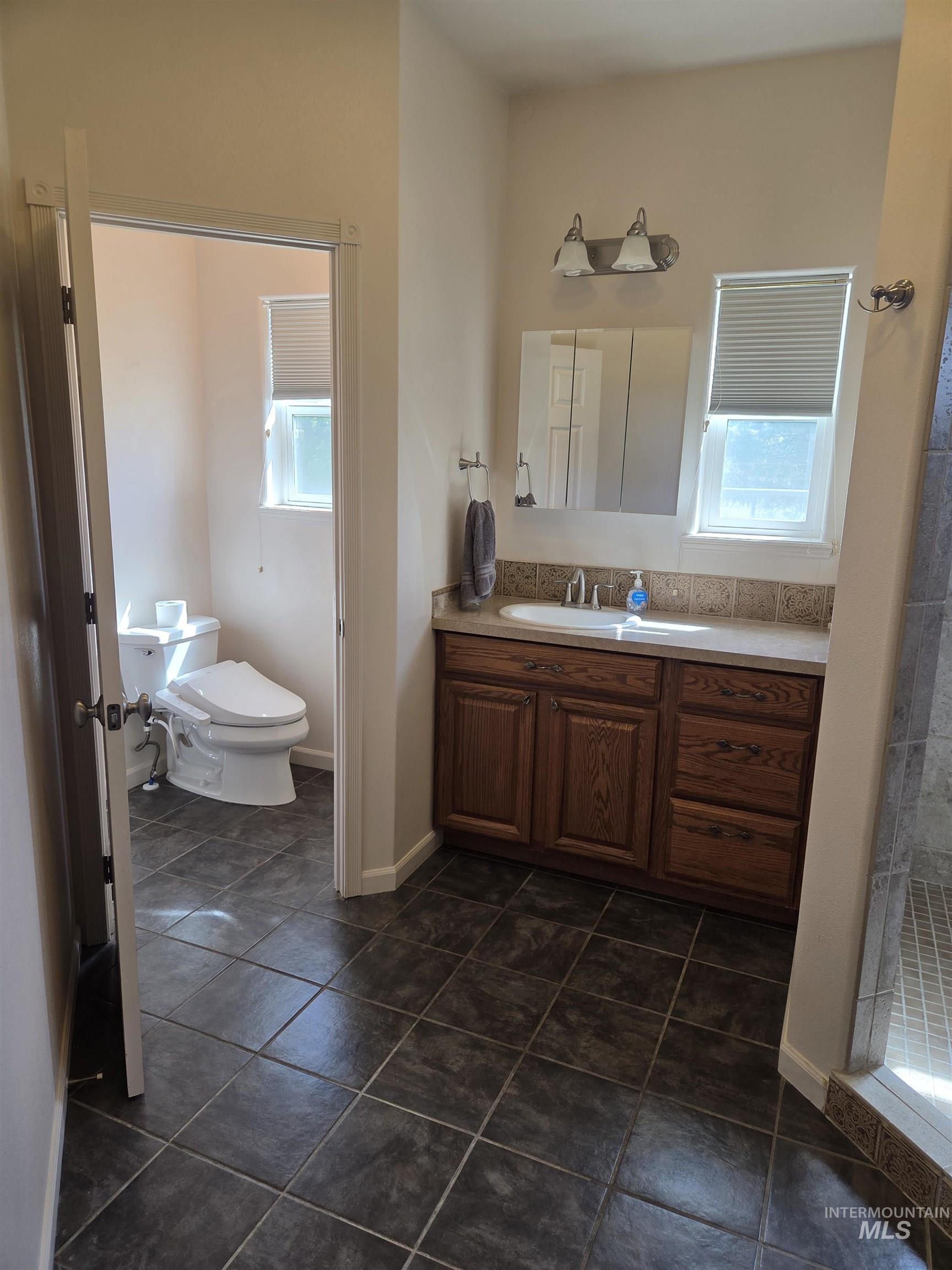 1085 Wallen Road Moscow, ID 83843 - Photo 26 of 50 Bathroom featuring dark square floor tiles, a wood-finish vanity with a light-toned countertop, and a tiled backsplash