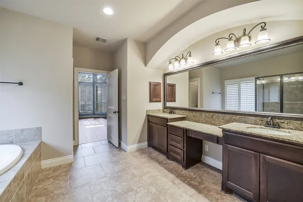 a spacious bathroom with a granite countertop double vanity sink a mirror and a bathtub