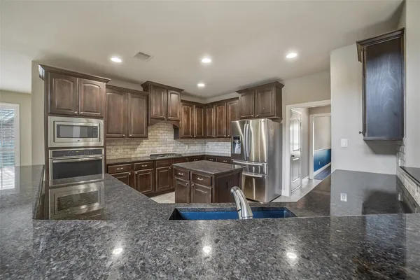 a kitchen with stainless steel appliances granite countertop a refrigerator a stove and a sink