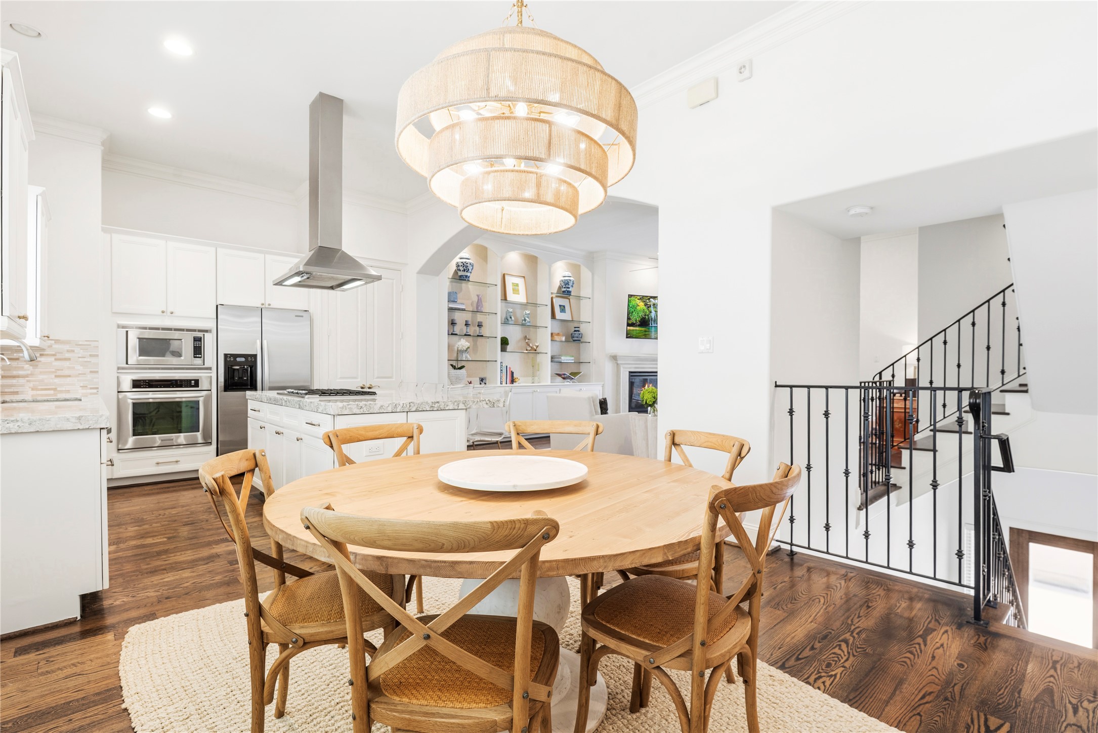 1537 Haddon Street Houston, TX 77006 - Photo 6 of 48 A bright, open kitchen and dining area with modern appliances, a central island, and elegant wooden flooring. The round dining table is complemented by a stylish light fixture above(excluded). The space flows into a cozy living area, and a staircase adding character to the layout.