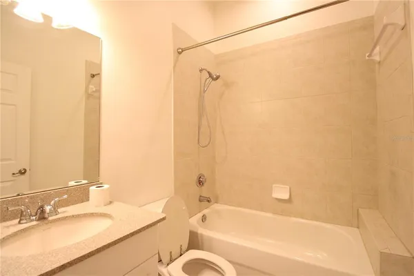 a bathroom with a granite countertop bathtub shower sink vanity and a toilet