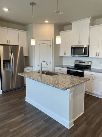 a kitchen with stainless steel appliances granite countertop a sink a stove a refrigerator and island with wooden floor