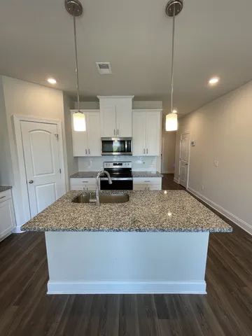 a kitchen with kitchen island granite countertop a sink a counter space appliances and cabinets
