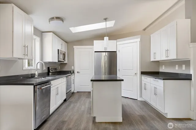 a kitchen with stainless steel appliances granite countertop a refrigerator a sink dishwasher a stove and white countertops with wooden floor