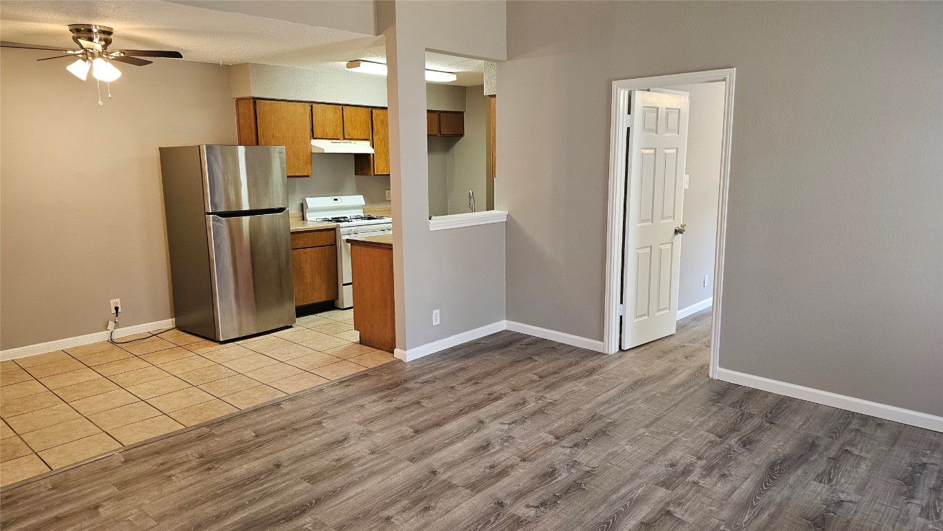 Kitchen featuring freestanding refrigerator, white range with gas cooktop, under cabinet range hood, brown cabinets, and ceiling fan
