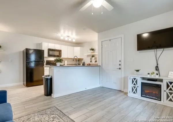a living room with stainless steel appliances furniture a fireplace a flat screen tv and view kitchen