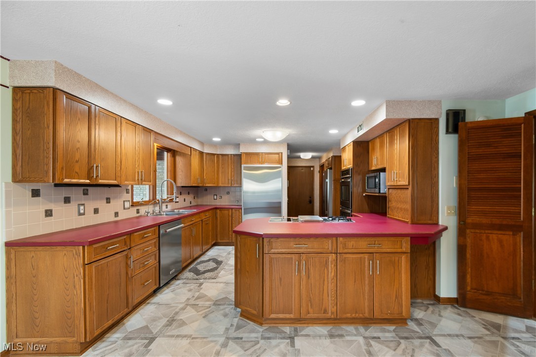 2317 Raintree Street Northeast Canton, OH 44705 - Photo 6 of 40 Kitchen with tasteful backsplash, brown cabinetry, appliances with stainless steel finishes, recessed lighting, and a peninsula