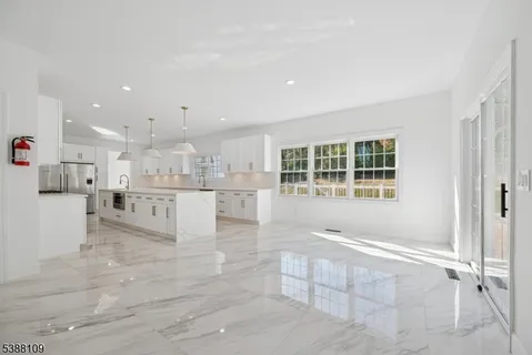 a large white kitchen with kitchen island a stove a sink dishwasher and white cabinets with wooden floor