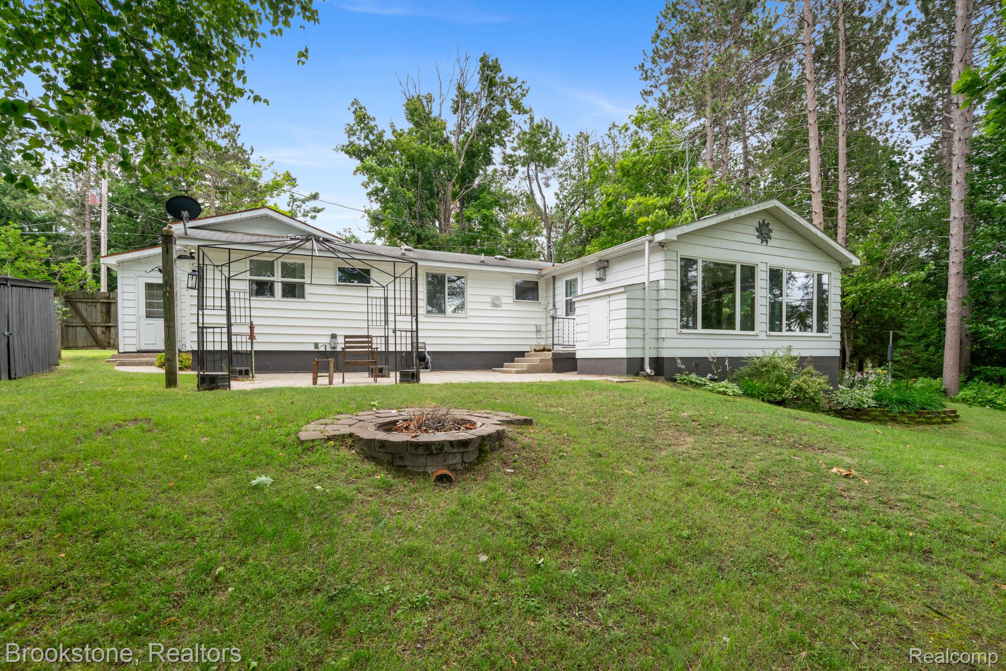5699 Smith Road Cheboygan, MI 49721 - Photo 1 of 30 Expansive backyard featuring a built-in fire pit, a paved patio with an open metal gazebo, and a sloped lawn