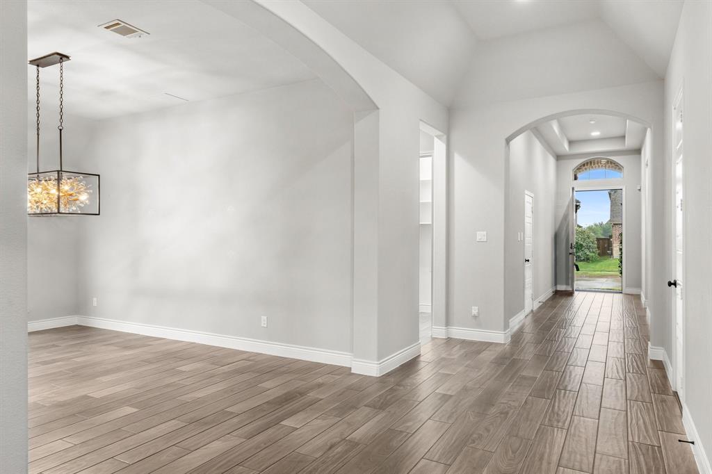 1501 Calcot Lane Forney, TX 75126 - Photo 4 of 34 Open-concept interior featuring wood-finish flooring, arched doorways, a coffered ceiling in the entry, crisp white baseboards, and a modern rectangular chandelier