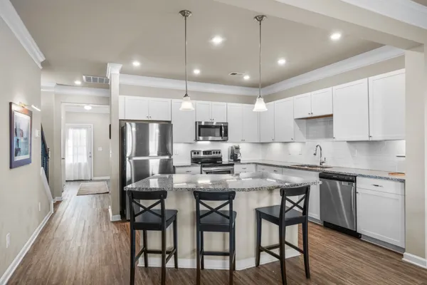 a kitchen with stainless steel appliances kitchen island granite countertop a dining table chairs refrigerator and microwave