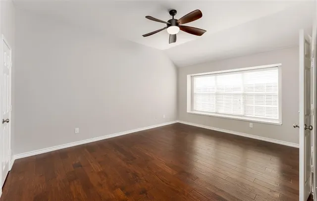 an empty room with wooden floor ceiling fan and windows