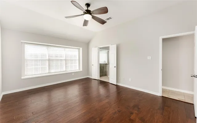 an empty room with wooden floor fan and windows