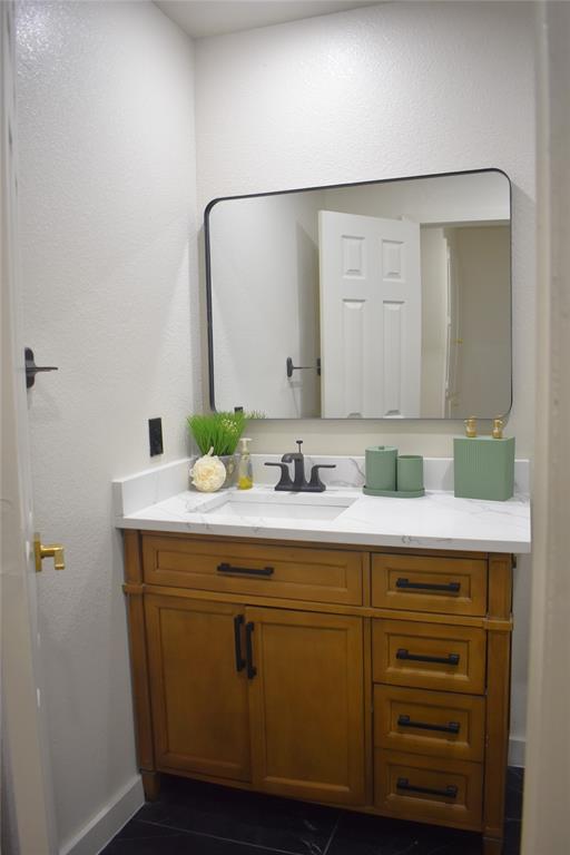 2908 Washington Street Commerce, TX 75428 - Photo 36 of 40 Bathroom vanity featuring a wood-finish cabinet, white countertop, integrated sink, and black fixtures