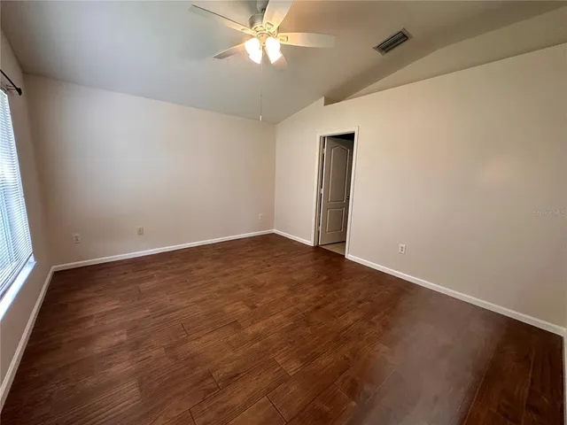 an empty room with wooden floor fan and windows