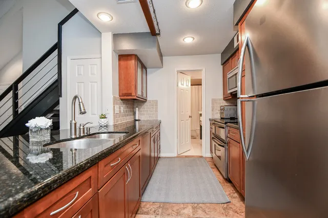a kitchen with granite countertop a refrigerator a sink and wooden cabinets