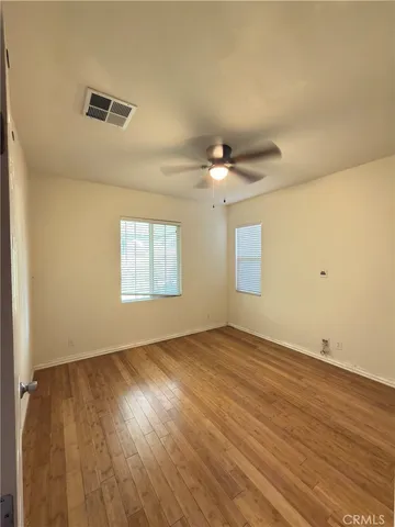 an empty room with wooden floor fan and windows