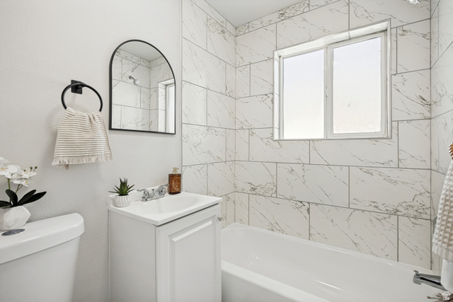 662 29th Street Ogden, UT 84403 - Photo 10 of 23 Bathroom featuring a white vanity with a single basin sink, an arched black-framed mirror, and a full bathtub with white subway tile surround
