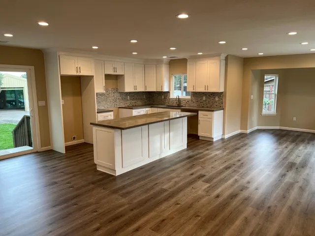 an open kitchen with kitchen island white cabinets wooden floor and center island